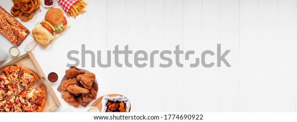 Selection of take out and\
fast foods. Corner border banner. Pizza, hamburgers, fried chicken\
and sides.  Top down view on a white wood background with copy\
space.