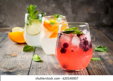 Selection of three kinds of gin tonic: with blackberries, with orange, with lime and mint leaves. In glasses on a rustic wooden background. Copy space  - Shutterstock ID 620140007