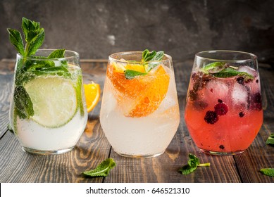Selection of three kinds of gin tonic: with blackberries, with orange, with lime and mint leaves. In glasses on a rustic wooden background. Copy space - Shutterstock ID 646521310