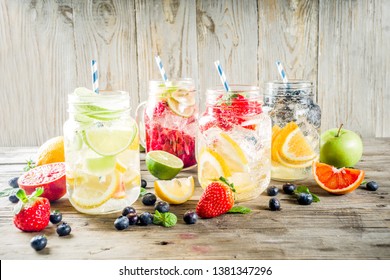 Selection various fruit and berry lemonade drinks, refreshment infused water, in mason jars, with fresh strawberry, lemon, lime, oranges, blueberry, wooden background copy space