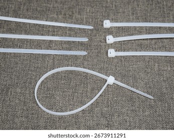 A selection of white plastic cable ties arranged on a textured gray background, with one tie fastened into a loop.