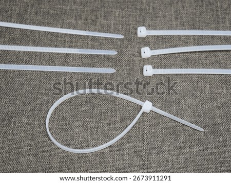 A selection of white plastic cable ties arranged on a textured gray background, with one tie fastened into a loop.