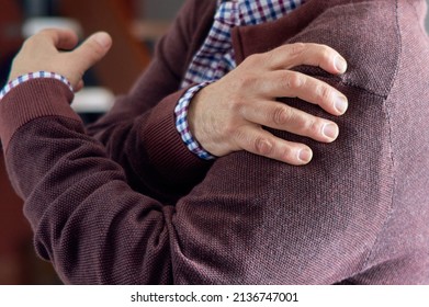 Selective blur. Horizontal photo. An older man puts his hand on his shoulder because he has pain due to osteoarthritis, arthritis, or rheumatism.