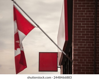 Selective blur on An empty red signboard of a retail shop poised for branding, with the Canadian flag waiving above, with a backdrop of a traditional brick wall, signifying business  national identit
