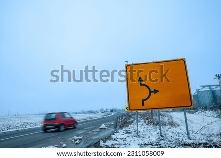 Selective blur on a fast car with a speed blur in winter, with a snowy rural environment, in a european road, with a blank yellow roadsign, in the serbian countryside.