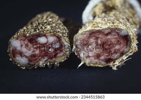 Selective blur on a macro shot of two fuet sausages coated in peppercorn and herbs, isolated on black background. Fuet, like to French saucisson, is spanish catalan dry cured sausage made of pork meat