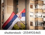 Selective blur on The Serbian flag waving against a backdrop of urban architecture in Belgrade, symbolizing national pride.