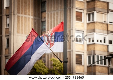 Selective blur on The Serbian flag waving against a backdrop of urban architecture in Belgrade, symbolizing national pride.