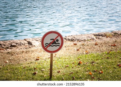 Selective blur on a standard no swimming sign on a lawn, in front of a water, a lake, indicating that it's forbidden to swim in these waters due to several dangers.  - Shutterstock ID 2152896135