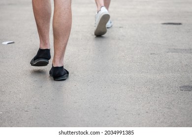 Selective Blur On Unrecognizable Legs And Feet Of Caucasian White Male Wearing Flip Flop Slippers Sandals With Black Socks. Flipflops And Socks Are A German Stereotype Considered As A Faux Pas. 

