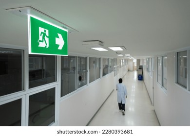 Selective fire exit sign on white ceiling.Green fire escape sign hang on the ceiling in the office.Fire fighting equipment concept.