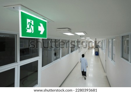 Selective fire exit sign on white ceiling.Green fire escape sign hang on the ceiling in the office.Fire fighting equipment concept.