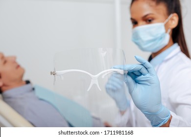 Selective Focus Of African American Dentist In Medical Mask Holding Face Shield Near Patient