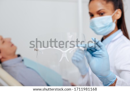selective focus of african american dentist in medical mask holding face shield near patient