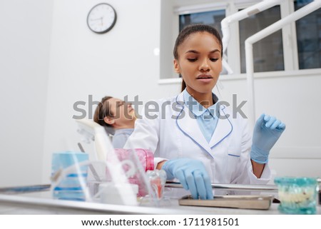 selective focus of african american dentist in latex gloves touching stainless dental instruments near patient