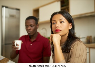 Selective Focus Of African Couple, Sitting At Kitchen In Morning, Man On Background Holding White Coffee Cup, Thoughtful Woman With Hand Under Chin, Contemplating, Getting Ready To Go For Work