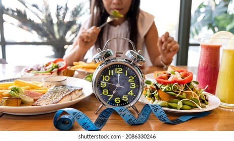 Selective focus of Alarm clock with woman eating a healthy food as Intermittent fasting, time-restricted eating - Shutterstock ID 2086330246