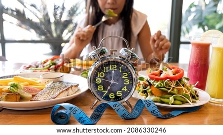 Selective focus of Alarm clock with woman eating a healthy food as Intermittent fasting, time-restricted eating