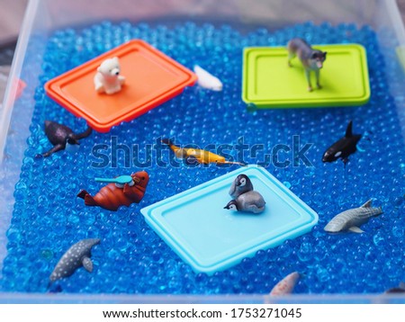 Selective focus of arctic animals mini figures in blue hydrogel water beads and colorful plastic plates as ice floe. Kids sensory play activities and education concept.