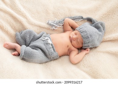 Selective Focus Of Asian Little Baby Sleeping On Back With His Hands Behind His Head On Beige Blanket, Adorable Toddler Wearing Knitted Gray Hat. Infant Sleeping On Bed With Happy And Safe.