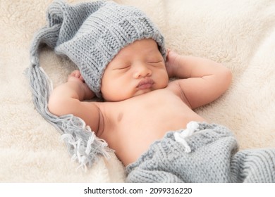 Selective Focus Of Asian Little Baby Sleeping On Back With His Hands Behind His Head On Beige Blanket, Adorable Toddler Wearing Knitted Gray Hat. Infant Sleeping On Bed With Happy And Safe.