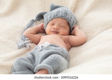 Selective Focus Of Asian Little Baby Sleeping On Back With His Hands Behind His Head On Beige Blanket, Adorable Toddler Wearing Knitted Gray Hat. Infant Sleeping On Bed With Happy And Safe.