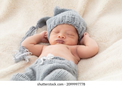 Selective Focus Of Asian Little Baby Sleeping On Back With His Hands Behind His Head On Beige Blanket, Adorable Toddler Wearing Knitted Gray Hat. Infant Sleeping On Bed With Happy And Safe.