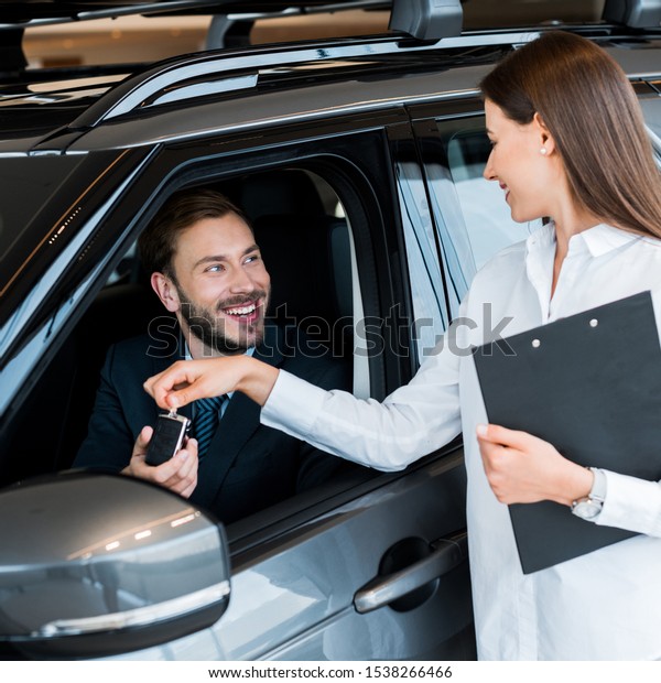 selective focus of attractive woman giving car key to\
happy man in car 