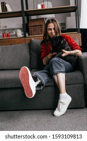 Selective Focus Of Attractive Woman With Leg Prosthesis Petting Pug Dog On Sofa