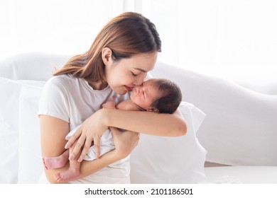 Selective Focus Of Beautiful Asian Mother Holding Newborn Baby In Bed. Happy Young Woman Holding And Kissing Adorable Infant With Love And Tender. Mom Spend Time Together With Toddler In Home.