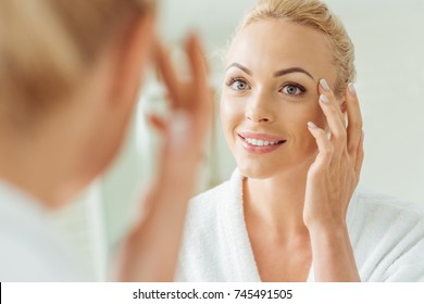 Selective Focus Of Beautiful Smiling Young Woman Touching Face While Looking At Mirror