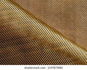 Selective Focus. The Bend Of The Golden Fabric Bulletproof Material Aramid. Aramid Kevlar Background. Golden Kevlar Texture And Pattern. Copy Space.