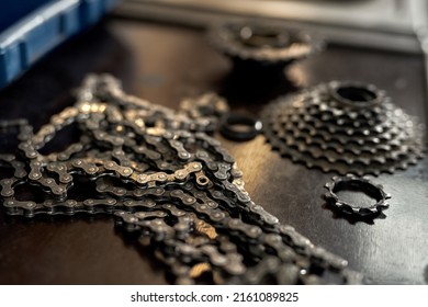 Selective Focus Of Bike Chain With Blurred Bicycle Cassette And Details For Broken Bike On Table In Workshop. Bike Service, Repair And Upgrade. Bicycle Fixing, Installing And Replacement