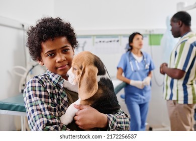 Selective focus of Black boy standing in vets office holding puppy, his grandpa and doctor talking about something on background