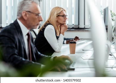 selective focus of blonde businesswoman looking at computer monitor near multicultural coworkers in office 
