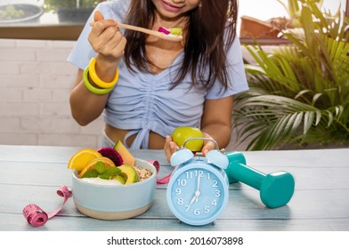  Selective Focus Of Blue Clock Which Woman Eating Healthy Of Yogurt Parfait With Intermittent Fast Program Day And Garden Background