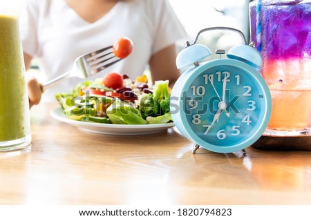Selective focus of blue clock which woman make a Intermittent fasting with  a Healthy food of salad .Healthy lifestyle Concept.