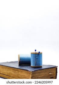 Selective focus of blue thread spools on bkue book over white background. Isolated 