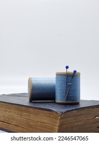 Selective focus of blue thread spools on bkue book over white background. Isolated 