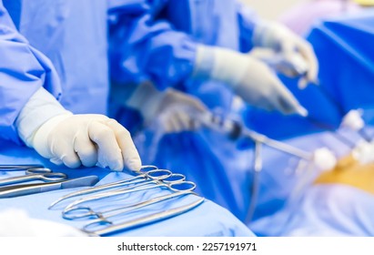 Selective focus with blur background. Scrub nurse picking up surgical instruments for surgeon inside operating room in modern hospital.Doctor in blue protective uniform doing laparoscopic surgery. - Powered by Shutterstock