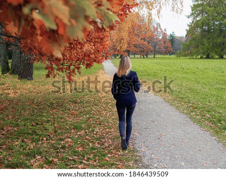 Selective focus. Blurred background. Backview of girl walking in the city park. Outdoor autumn portrait of young womann standing backwards with straight blond hair. forest nature at fall. 