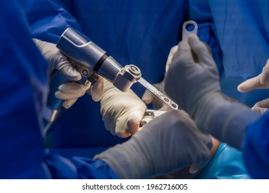 Selective Focus With Blurred Background.Orthopedic Surgeon In Blue Surgical Gown Suite Using Saw To Cut The Bone While Total Knee Replacement Surgery In Osteoarthritis Patient.Team Of Surgeons.