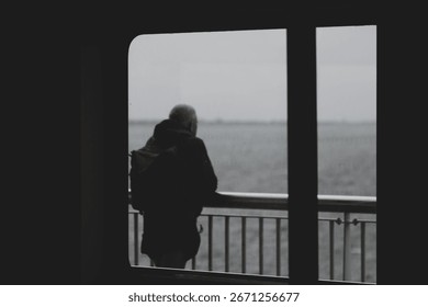 Selective focus of boat window frame with rain and cloudy in dark tone, Silhouette of a man standing on balcony of the ferry looking outside view, Blurred passenger in public transportation background