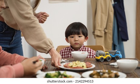 Selective Focus Of Bored Asian Baby Boy With Toy Cars Looking At The Dish Served By His Mother On Dinner Table. Child Eating Habit And Nutrition Concept