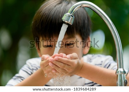 Selective focus at boy hands taking water from modern faucet in home garden.