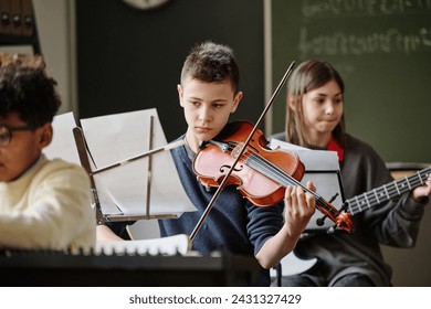 Selective focus of boy reading sheet music and playing violin during practice with school orchestra - Powered by Shutterstock