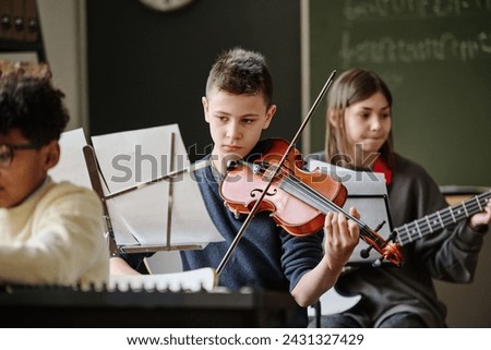 Selective focus of boy reading sheet music and playing violin during practice with school orchestra