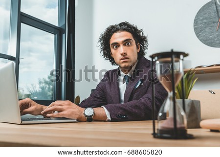 selective focus of businessman working on laptop and looking at sand clock while struggling to meet deadlines