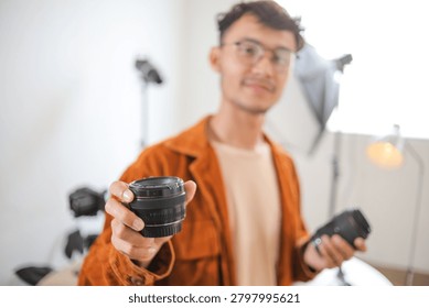 Selective Focus of Camera Lens Held by Blurred Asian Photographer in Photo Studio