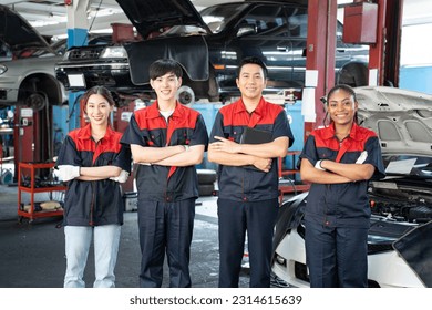 Selective focus of car mechanic team with African woman, two Asian men and a woman, in uniforms, standing with arms folded and smiling at camera with cars waiting for repairs in background at garage. - Powered by Shutterstock